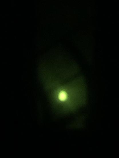 Blurry photo of eclipsed sun behind a cloud, in green hues caused by darkened glass.