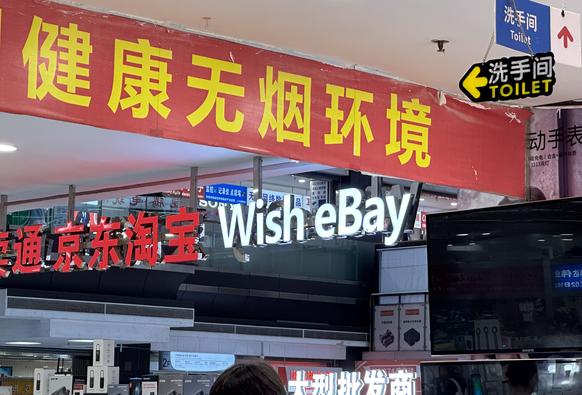 Zwischen chinesischen Schildern hängt eine Leuchtschrift auf der "Wish eBay" steht.