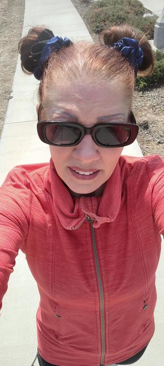 An awkward selfie of me walking in my peach jacket buns sunglasses