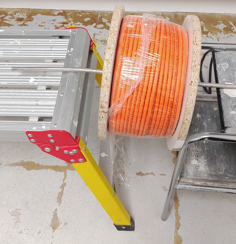 Cable reel mounted on a spare piece of 10mm solid steel wire (used in electrical installation for the earthing system) 
The bar sits loosely on two step stools and can roll off if tugged hard. Don't do this at work or your OSH inspector will get mad. 😉