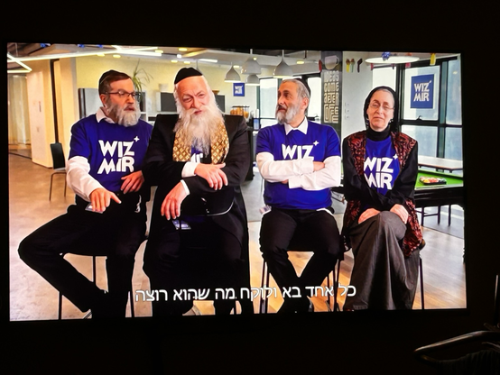Fernsehbild. Drei religiöse Männer und eine Frau mit T-Shirts mit Logo „Wiz Mir“