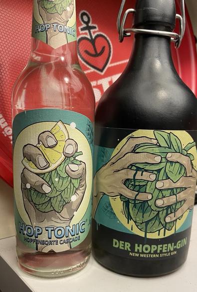 Links eine schlanke Flasche „Hop Tonic“ Tonic Water aus der Hopfensorte Cascade. Rechts daneben eine etwas gedrungene Flasche „Hopfen-Gin“.