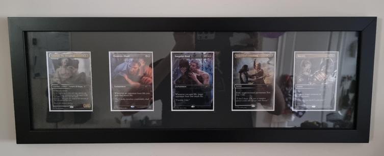 Photo of 5 Astarion themed holographic magic the gathering cards that are framed and hanging on a wall. In the reflection on the frame glass, you can see the person taking the photo with their phone.