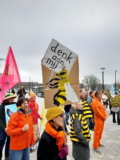 A person holding up a protest sign with a painting of a bee that is also holding up a sign that says "Think of me"