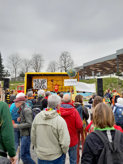 People gathered in front of a stage. To the left is a protest sign that says "This is a dead end" and to the right a globe on a stick with underneath it a sign that says "I fear a habitable earth".