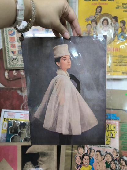 a magazine page with a full photo of Audrey Hepburn in a tall white hat and sheer white cape with black gloves