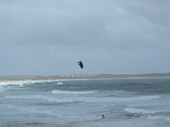The image depicts a coastal scene with a wide sandy beach in the foreground. The beach is bordered by a line of green vegetation, likely dunes, which extends into the distance. The ocean is visible with waves breaking near the shore, creating white foam. The sky is overcast with gray clouds, suggesting a gloomy or stormy weather condition. The overall color palette is muted, with shades of gray, blue, and green dominating the scene. There are no visible people or man-made structures, giving the image a natural and serene appearance.
―
The image depicts a coastal scene with a cloudy sky and choppy ocean waves. In the foreground, a person is kite surfing, visible as a small figure in the water, with a black kite flying above them. The kite is positioned in the center of the image, slightly above the horizon line. The ocean is a mix of dark and light blue hues, with white foam on the waves, indicating strong winds. In the background, a sandy beach is visible, with some buildings and vegetation along the shoreline. The overall atmosphere is overcast, with a grayish-blue sky filled with clouds, suggesting a windy day suitable for kite surfing.

Provided by @altbot
