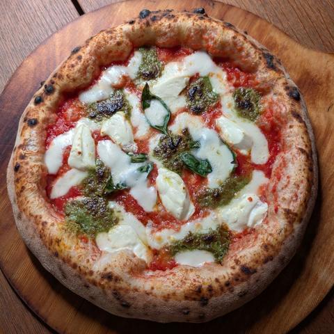 A Pizza Napoletana with an big and airy crust on a wooden plate. It's topped with pistachio pesto and Mascarpone.