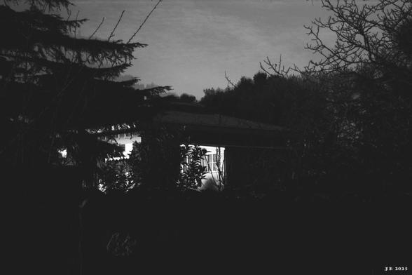 Dunkles Schwarzweißfoto außerhalb von Falcognana, Lazio, Italien. Von einem Haus, das von Wald umgeben ist, ist nur der beleuchtete Teil fast weiß sichtbar. Oben im Bild grauer Himmel. Leica Z2X auf Afga Copex Rapid-Film.