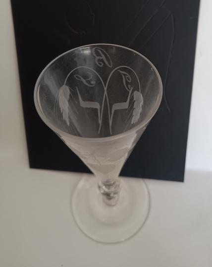 The same glass, viewed from above with a black background to show the engraved 'ears' of barley and the owner's initials.