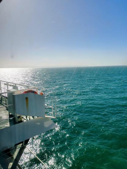 Seascape view taken from the panoramic lounge looking out over the starboard foredeck to the French shoreline in the distance. The sky is cloudless and the green blue sea shimmers in the sunlight.