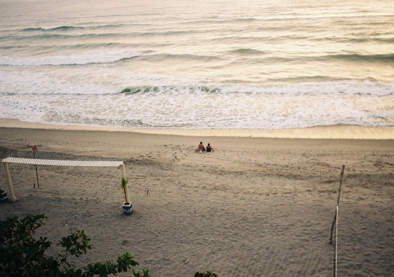 Two people sitting by the shore on the beach.