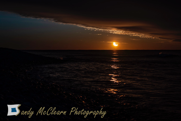 Partial solar eclipse rising above the sea beneath the cloud deck.