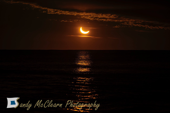 Partial solar eclipse rising above the sea beneath the cloud deck.