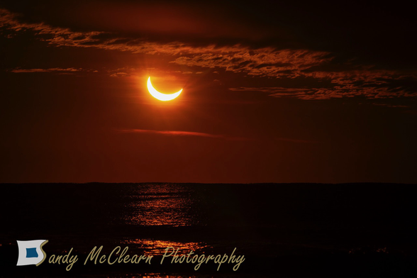 Partial solar eclipse rising above the sea beneath the cloud deck.