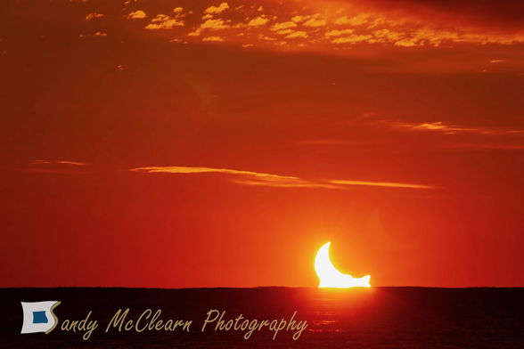 Partial solar eclipse rising above the sea beneath the cloud deck.