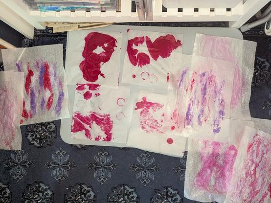 Ten 9x12" sheets of medical exam table paper and rice paper, spread out on my studio floor, mostly on a polyethylene desk protector. All bear messy, abstract shapes in red, pink, white and light purple - streaks, dendrities, and the un-planned red ink blots of course 🤭

Under all that is my lovely, dark denim blue turkish rug with a dusty looking repeating medallion pattern (the more elaborate patterns are at the borders :-).

This is the west half of my kitchen, by the way. I'm a much better artist than a cook 🤭 (and that's not saying much, in fact 🤣)