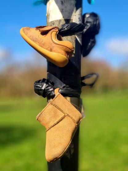 Two kids shoes, of different design and sizes, tied to a post in a park.