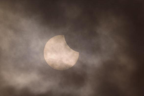 DE: Ein Bild der partiellen Sonnenfinsternis vom 29. März 2025. Der Mond verdeckt ein knappes Fünftel der Sonne am rechten, oberen Rand. Es war bewölkt, weswegen dunkle Schleier über die Sonne ziehen und ihr eine hübsche nebelige Umrandung geben.

EN: An image of the partial solar eclipse on 29 March 2025, with the moon obscuring just under a fifth of the sun at the top right-hand edge. It was cloudy, which is why a dark veil covers the sun and gives it a pretty foggy outline.