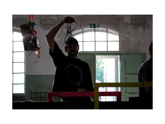 young musician setting up electronic music gear in an abandoned industrial site, holding a bunch of cables in the air
