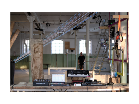 view of electronic music gear at a music stage in an abandoned industrial site with wooden structures and festival like decorations