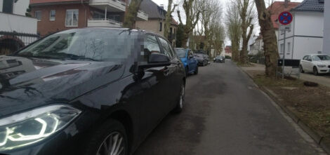 In einer Straße kommt ein Autp entgegen. Auf dessen Seite parken weitere Fahrzeuge, trotzdem wird daran vorbei gefahren und keine Rücksicht auf den vorrangigen Radverkehr genommen. Das Bild ist mit einer leicht außermittig am Lenker montierten Kamera aufgenommen.