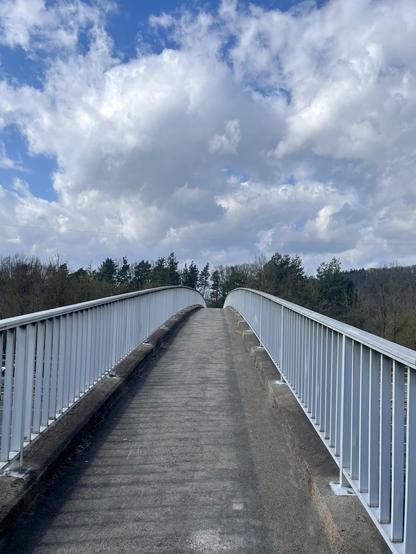 A narrow bridge for cyclists and pedestrians facing the blue sky with some white clouds.