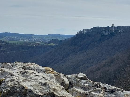 Über einen Felsblock streift der Blick über ein Tal, auf der Hügelkette ist der Turm von Schloß Lichtenstein zu sehen.
