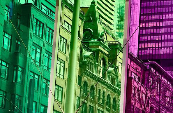 View of many different building types, ranging from Victorian to glass-and-steel high-rise, through the green, yellow and pink coloured glass of the Palais des Congrès convention centre in Montreal Canada.