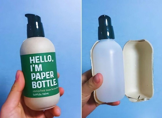 L'immagine mostra una bottiglia di innisfree Green Tea Scrub con un design innovativo. A sinistra, una mano tiene la bottiglia, che ha un'etichetta verde con il testo "HELLO, I'M PAPER BOTTLE." e "innisfree Green Tea Scrub 5.41FL.Oz./160mL." La bottiglia è bianca con un tappo nero a pompa. A destra, la stessa bottiglia è mostrata con la sua parte superiore rimossa, rivelando un contenitore di carta beige che funge da custodia. La bottiglia è vuota, e il contenitore di carta è aperto, mostrando la sua forma e struttura di plastica.