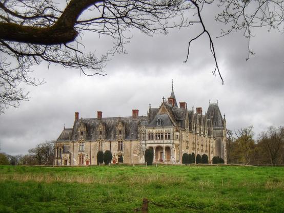 Un petit château bordé de pelouse. Le ciel est nuageux.