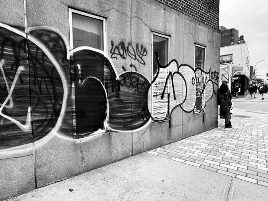 Black and White photography showing a street corner in Montreal where someone is resting on the wall of a building, covered with tags.