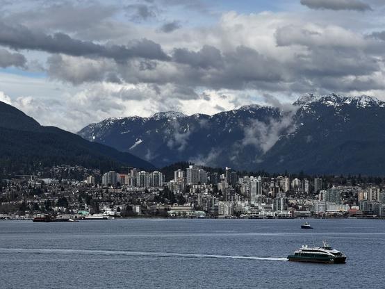 North Vancouver skyline from Canada Place. You can see mountains in the background, the city in the middle and the bay in the foreground with a ferry. 
- - -
L’horizon de North Vancouver vue à partir de la place du Canada. On peut voir les montagnes en arrière-plan, la ville au milieu et la baie au premier plan avec un traversier.