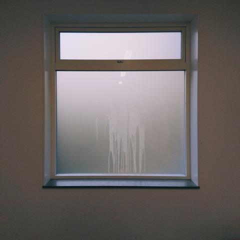 A frosted glass window with streaks of some liquid, framed in white and set in a plain wall.