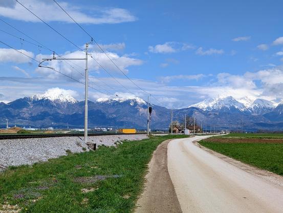 Road leading towards snow-covered mountains, railway at thd left.