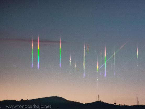 Atardecer. Desde el Carmel (Barcelona) Se ve el perfil de la sierra de Collserola a contraluz con algunas pequeñas torretas eléctricas en la cima. Sobre el cielo finas líneas verticales cada una con los colores del arcoiris.