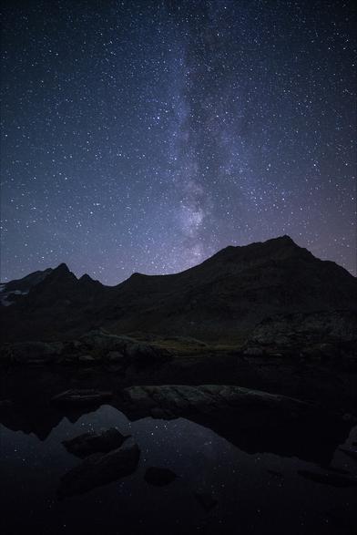 Photo d'un paysage de montagne nocturne au format portrait.
Un petit lac reflète le ciel étoilé et la silhouette des montagnes. Quelques cailloux trempent dans l'eau. Partant droit à la verticale de la plus haute montagne, la voie lactée traverse le ciel de bas en haut. 
Le lac occupe le quart inférieur de l'image, le ciel la moitié supérieure.
-
Portrait of a mountain landscape at night.
A small lake reflects the starry sky and the silhouette of the mountains. A few pebbles dip in the water. Stretching vertically from the highest mountain, the Milky Way crosses the sky from bottom to top. 
The lake occupies the lower quarter of the image, the sky the upper half.
