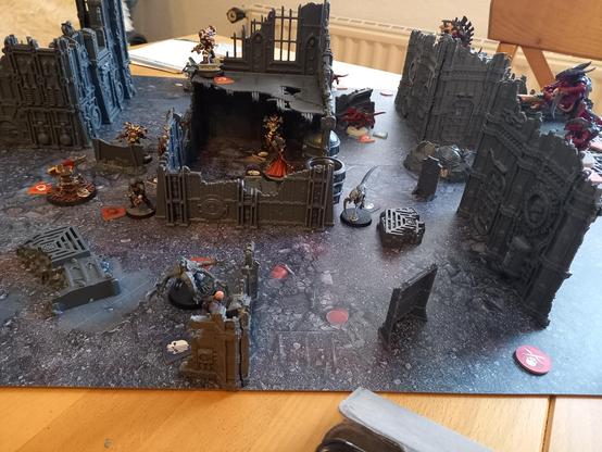 Ein aufgebautes Set des Tabletop-Games Killteam: mehrere Terrainteile, die Gebäuderuinen nachahmen und zwischen denen sich Miniaturen verbergen.