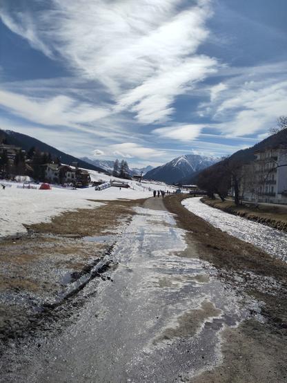 Foto. Berglandschaft mit einem von Schmelzwasser bedeckten Strässchen.