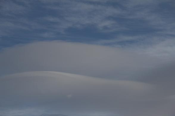 Foto vom Himmel mit zwei übereinandergelagerte Cumulus lenticularis Wolken. Beide Wolken haben eine ähnliche gewellte Form. Darüber ist blauer Himmel mit etwas Zirrus Wolken.
