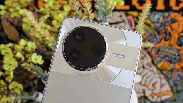 Picture of silver Poco F7 Pro camera pod with yellow flowers and orange poster out of focus in the background