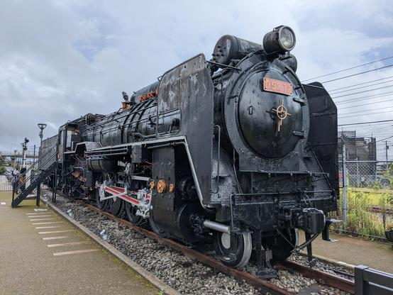 Schwarzes Dampflok Denkmal auf ein Stück geschotterte Schiene gesetzt.
Auf dem Typenschild an der Front steht die Bezeichnung "D 52 72"
Am Führerstand ist eine schwarze Metalltreppe angestellt.