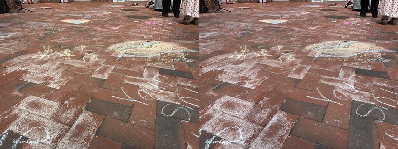 A view of sidewalk chalk art and messages across a large area of brick paving. Side-by-side parallel viewing 3D view.