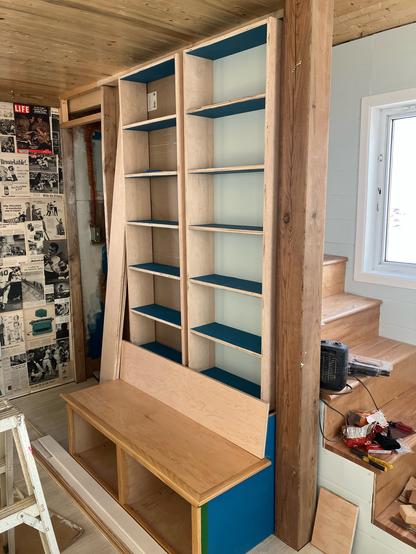 Shelves being built into a wall above a bench in a cabin.