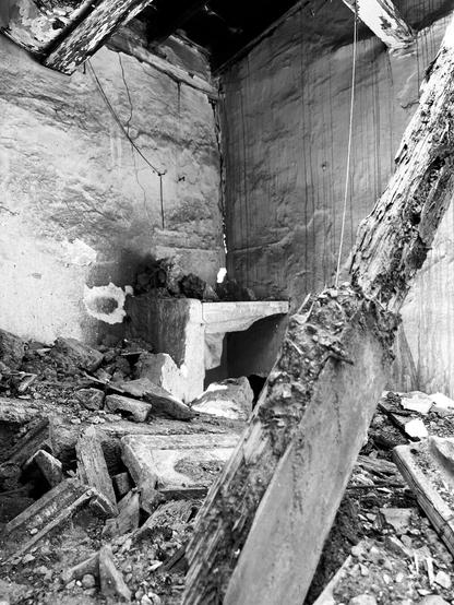 Black and white photograph.
In the corner of a collapsed room, tiles and rotten beams all over the floor, a square stone sink, intact, almost luminous.
