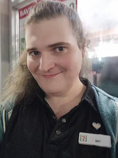 me at work with my trans pride heart pin on over my name tag