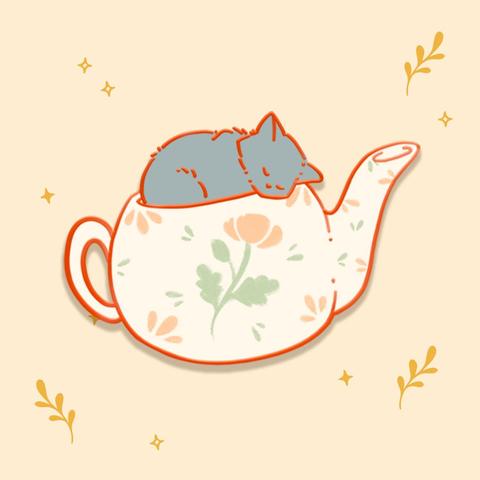 An illustration of a copper enamel pin of a cream teapot with a grey kitten sleeping inside of it. The teapot is decorated with leaves and a flower in soft green and pink designs.