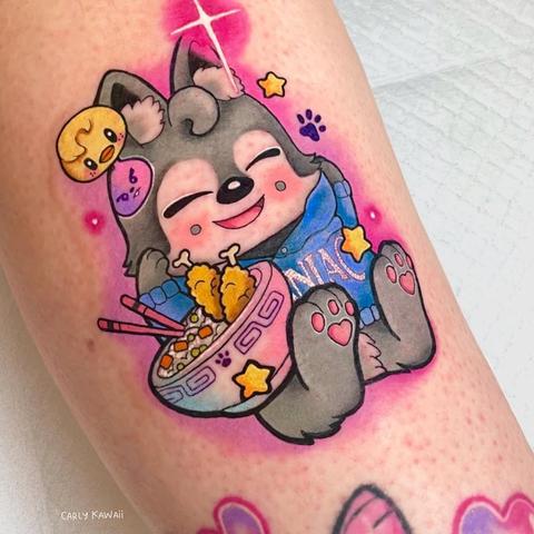 Colorful tattoo of Wolf Chan wearing a Maniac hoodie, with a bowl of food in front of him. He has Bbokari and Leebit decals near one of his ears.