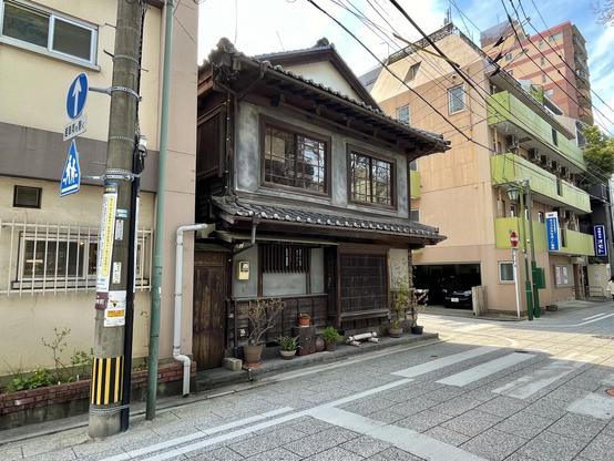 A traditional Japanese house in a street corner, with several potted plants against the wall.