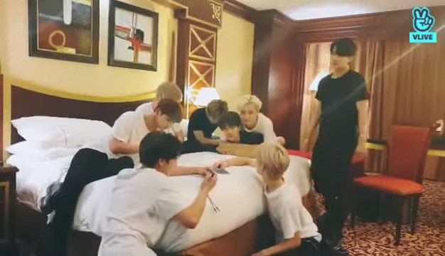 skz in a hotel room. Seungmin is bent over the edge of the bed. Chan is fully on top of him with his arms wrapped around Seungmin's shoulders, preventing Seungmin from moving his arms. Both are looking at the camera. There's an air of 'welp I guess this is happening now'